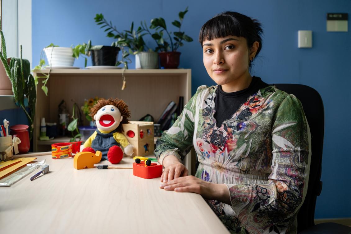 Karla Perez seated at a table. On the table are a doll and several other children's toys used in early childhood cognition studies.