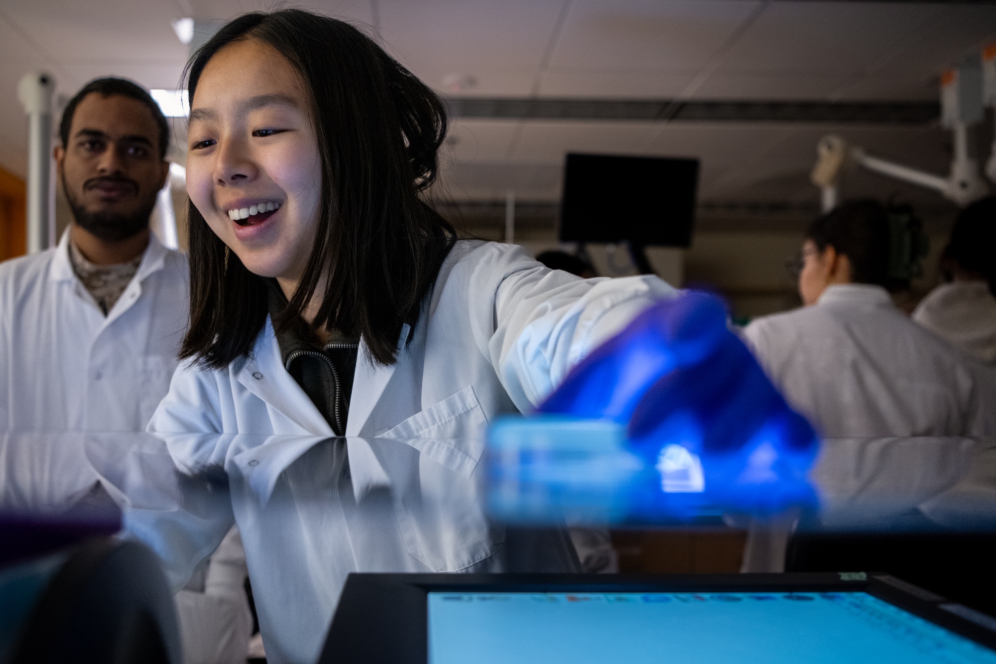 Two people in lab coats perform testing with a machine.