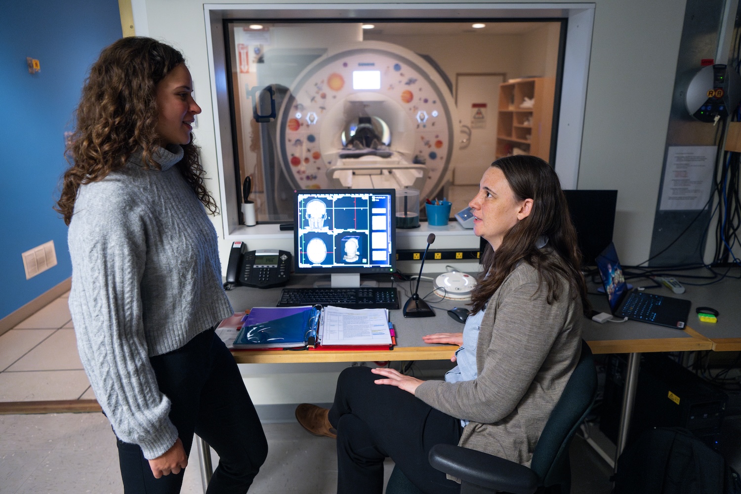 Two people speaking in front of a monitor for an MRI