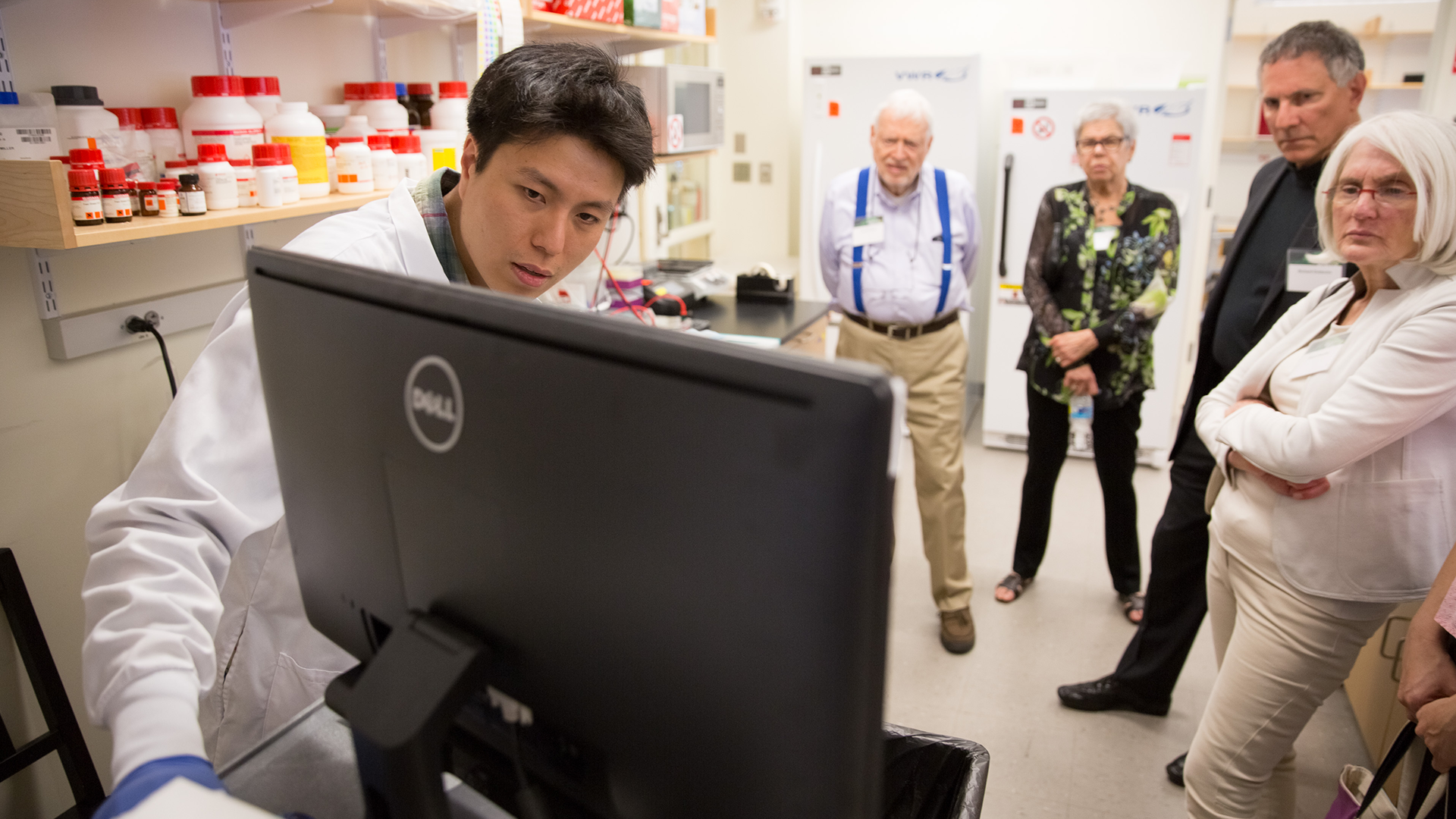 a graduate student points to a computer screen and explains his research to visitors