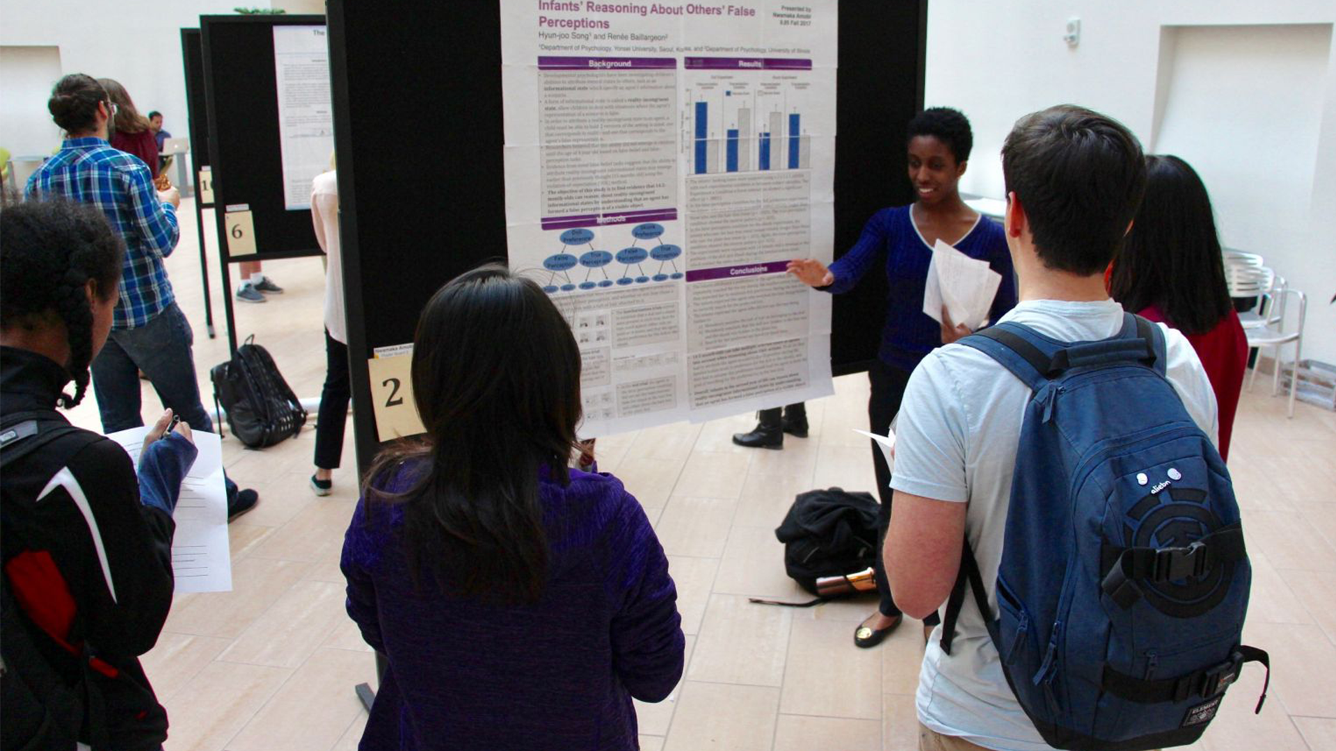 a female student explains her research poster to several other people