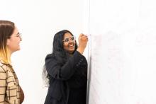 Nidhi Seethapathi writes on a white board while a colleague looks on.